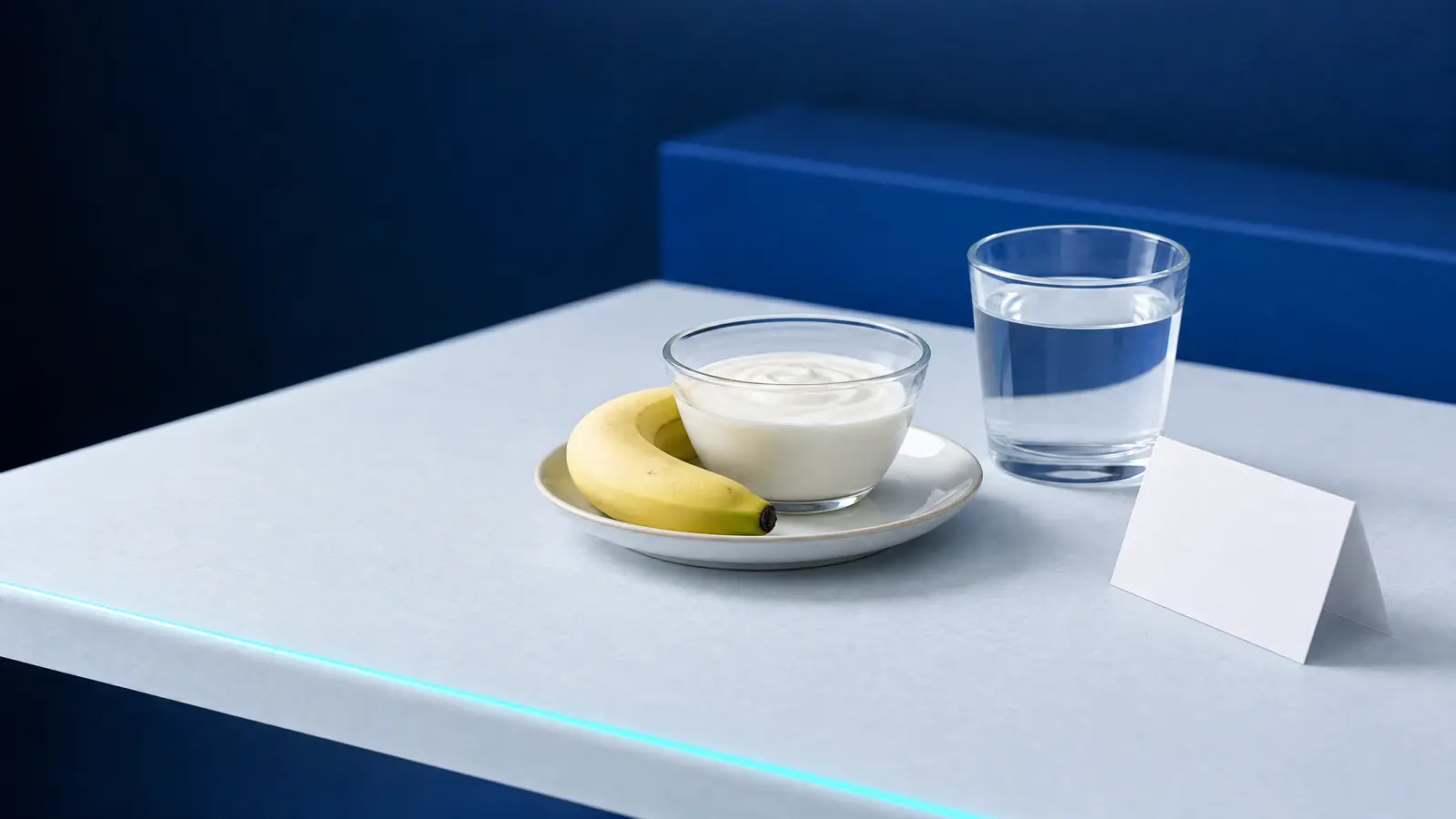 Ein Teller mit Naturjoghurt und einer Banane, ein Glas Wasser und eine leere gefaltete Karte