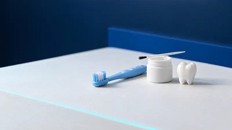 A children's toothbrush, a small pot of fluoride varnish with a brush and a ceramic tooth model