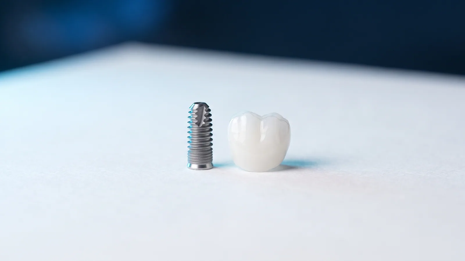 A titanium dental implant and a white zirconia crown standing side by side on a light surface